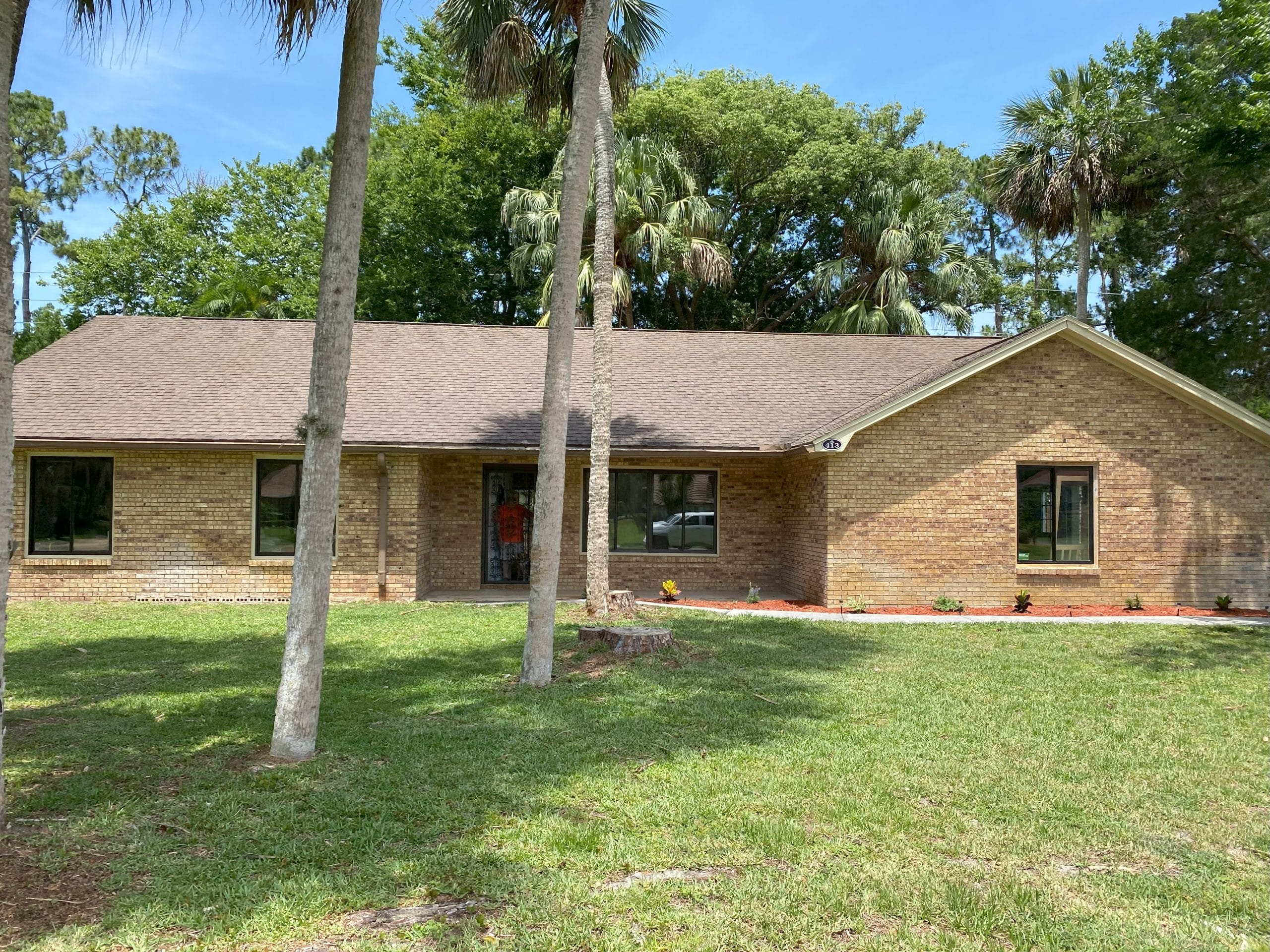 Port Orange Residential Pressure Cleaning Company A single-story brick house with a brown shingle roof, surrounded by palm trees and a well-maintained lawn.